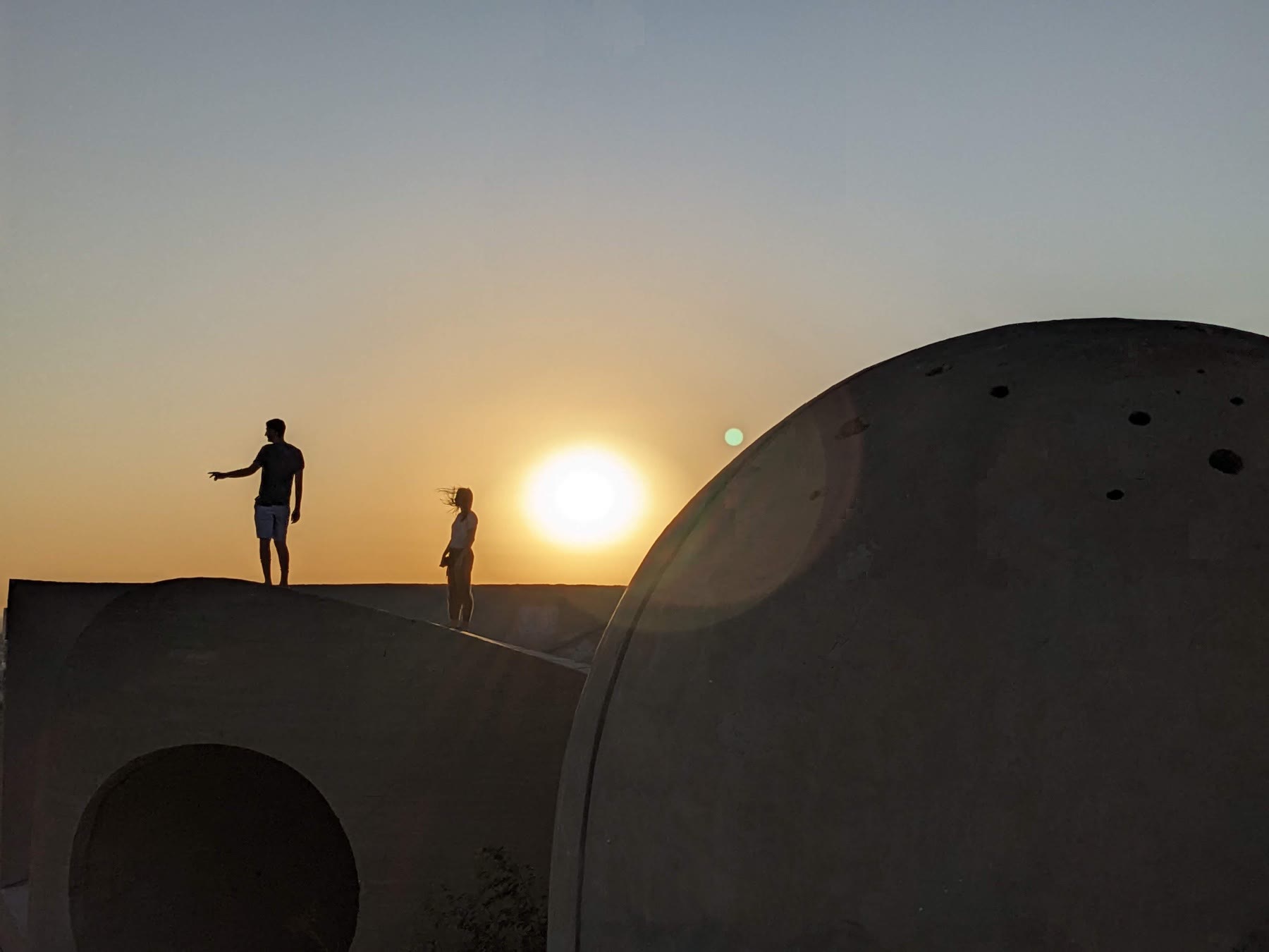 Desert structure at sunset with people standing near a dome